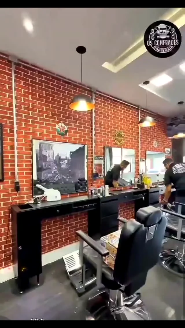 Interior real da Os Confrades Barbearia com cadeiras, espelhos e parede de tijolos